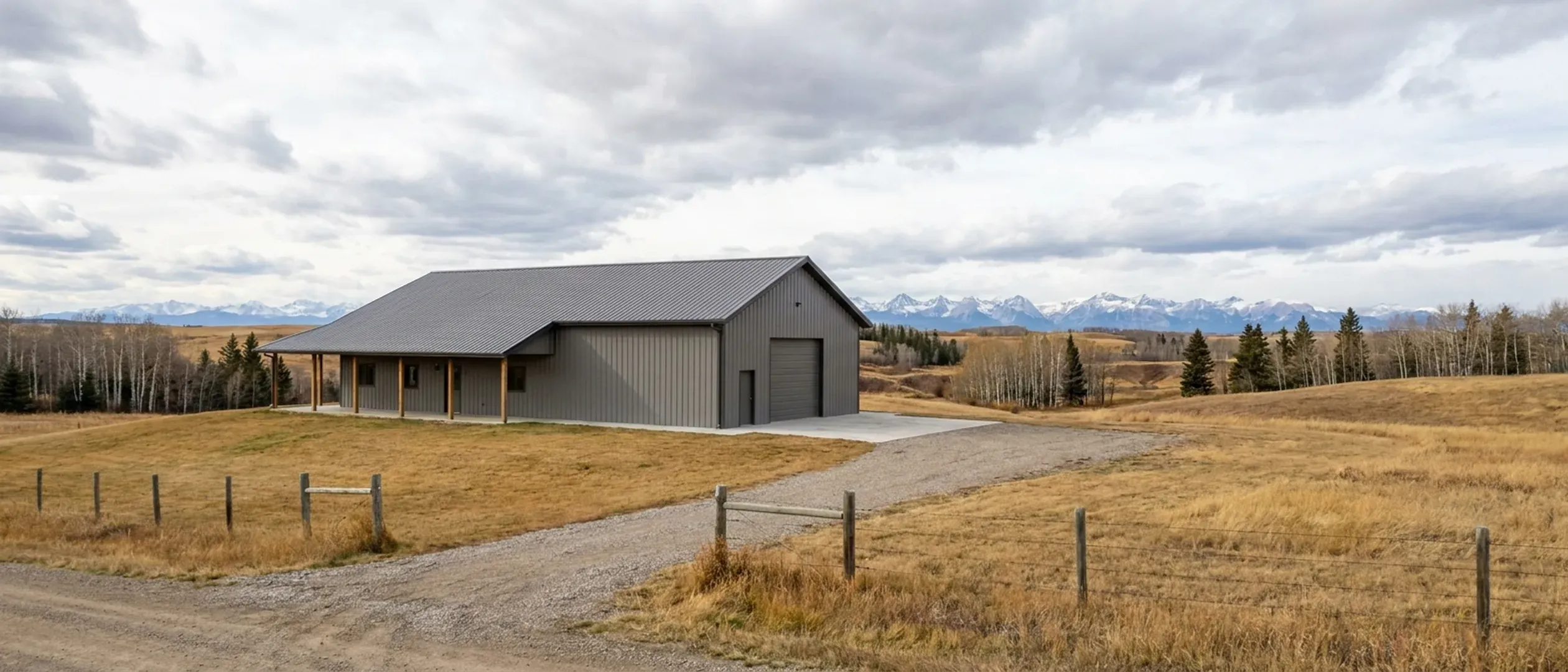 A completed barndominium with a covered entry porch and an attached shop bay, photographed in flat overcast daylight on rolling grassland.